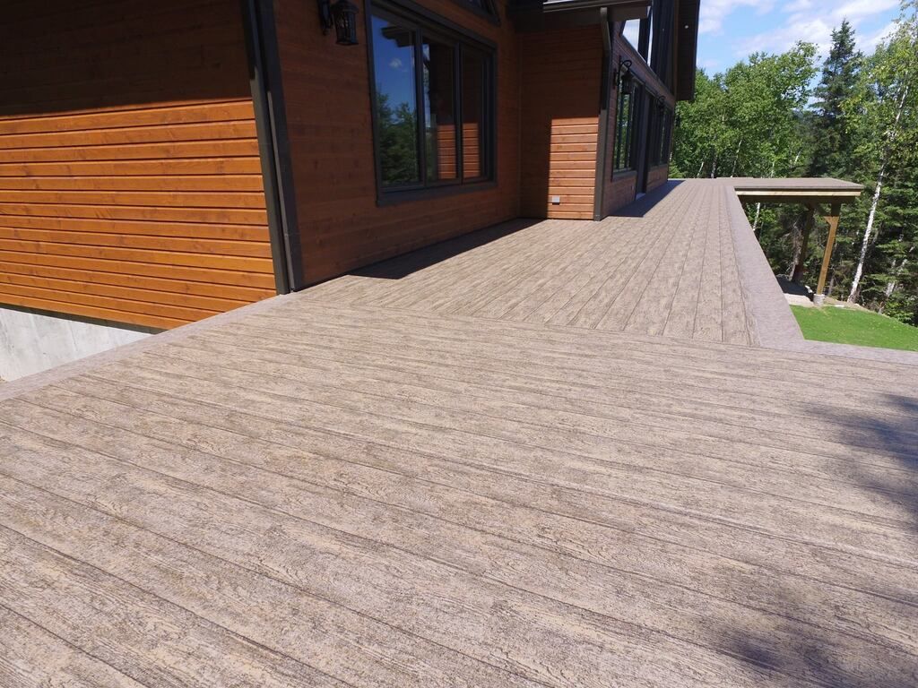 Une grande terrasse en membrane de pvc avec une maison en bois en arrière-plan