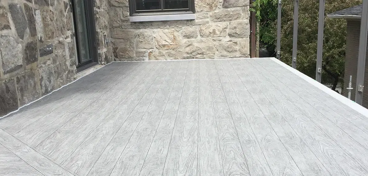 Patio recouverte d'un revêtement de pvc gris à côté d'une maison en pierre