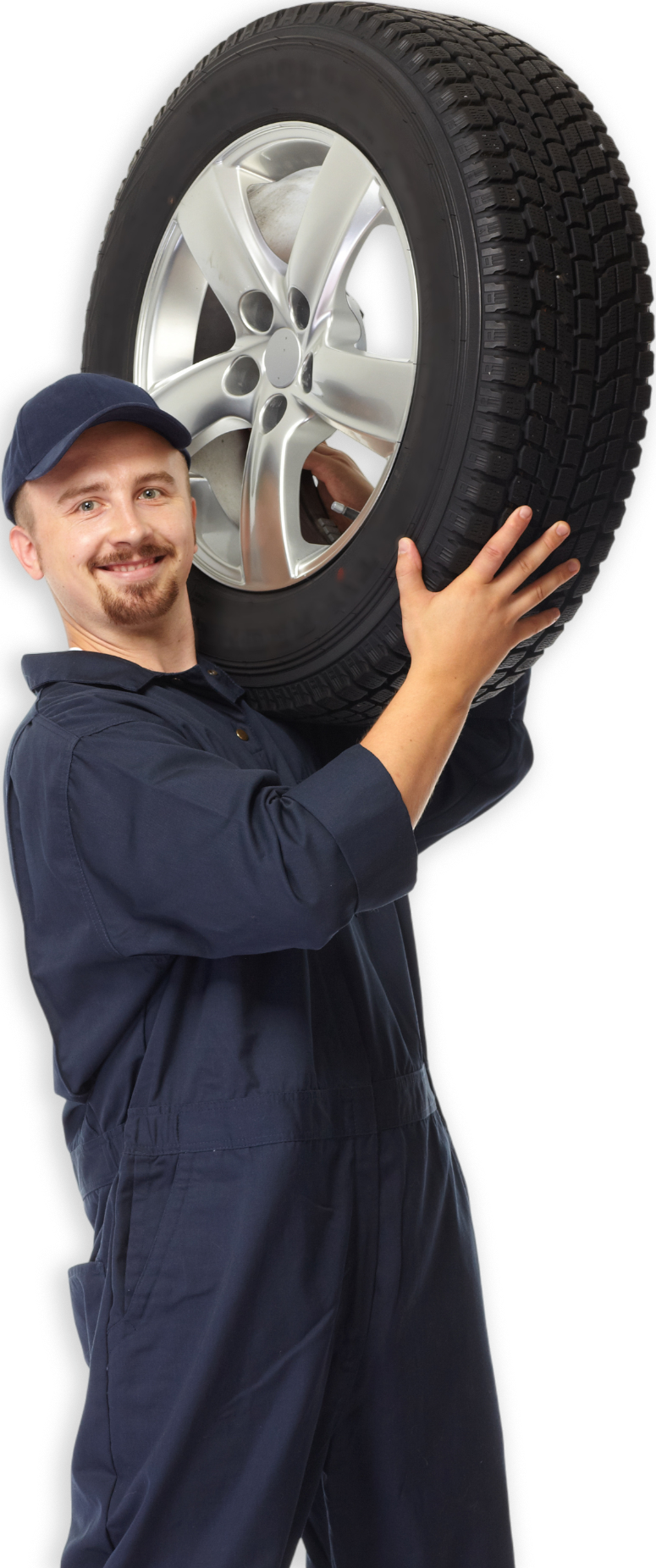 Mechanic in blue jumpsuit carries a tire over his shoulder, smiling.