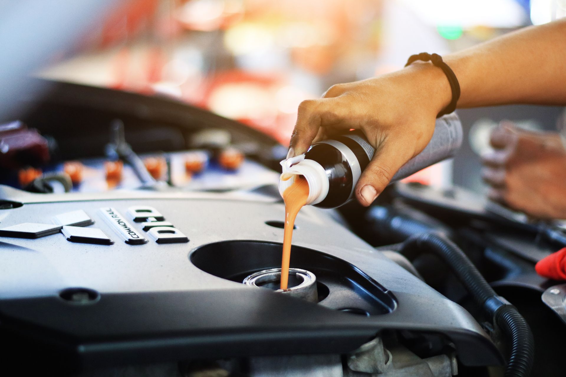 Hand pouring liquid from a bottle into a car engine, suggesting maintenance.