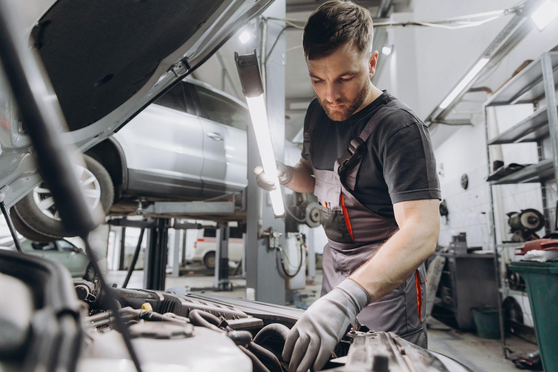 Mechanic examining car engine with a light in a garage.