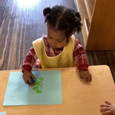 A little girl is sitting at a table playing with paint