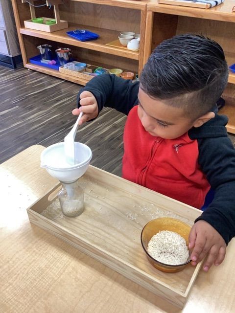 A young boy is pouring something into a bowl with a spoon