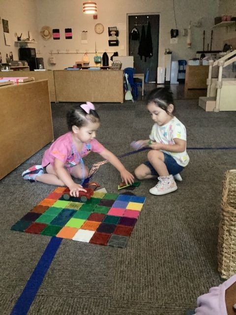 Two little girls are sitting on the floor playing with blocks