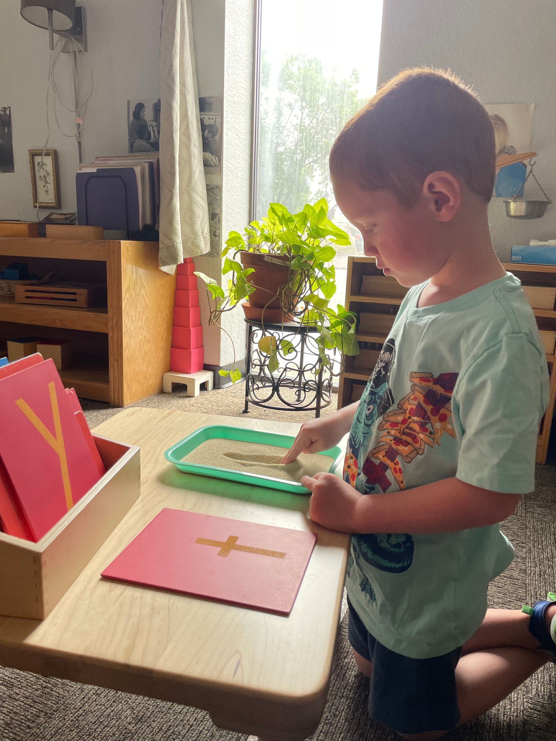 A young boy is kneeling down at a table playing with sand.