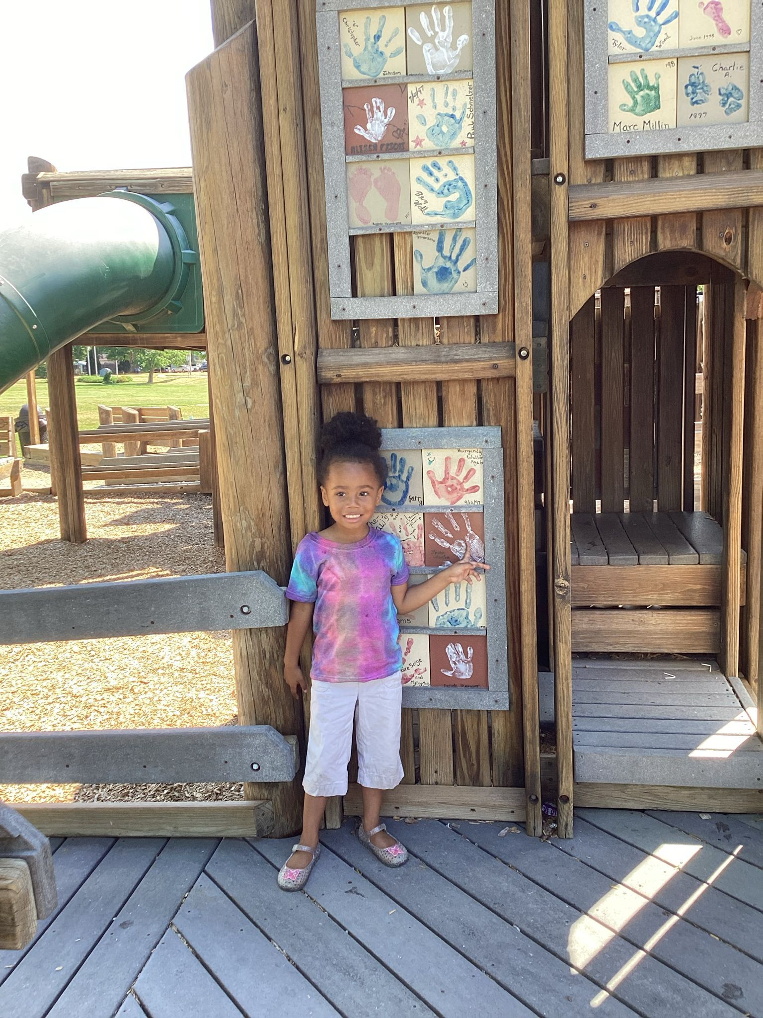 A little girl is standing in front of a wooden playground.