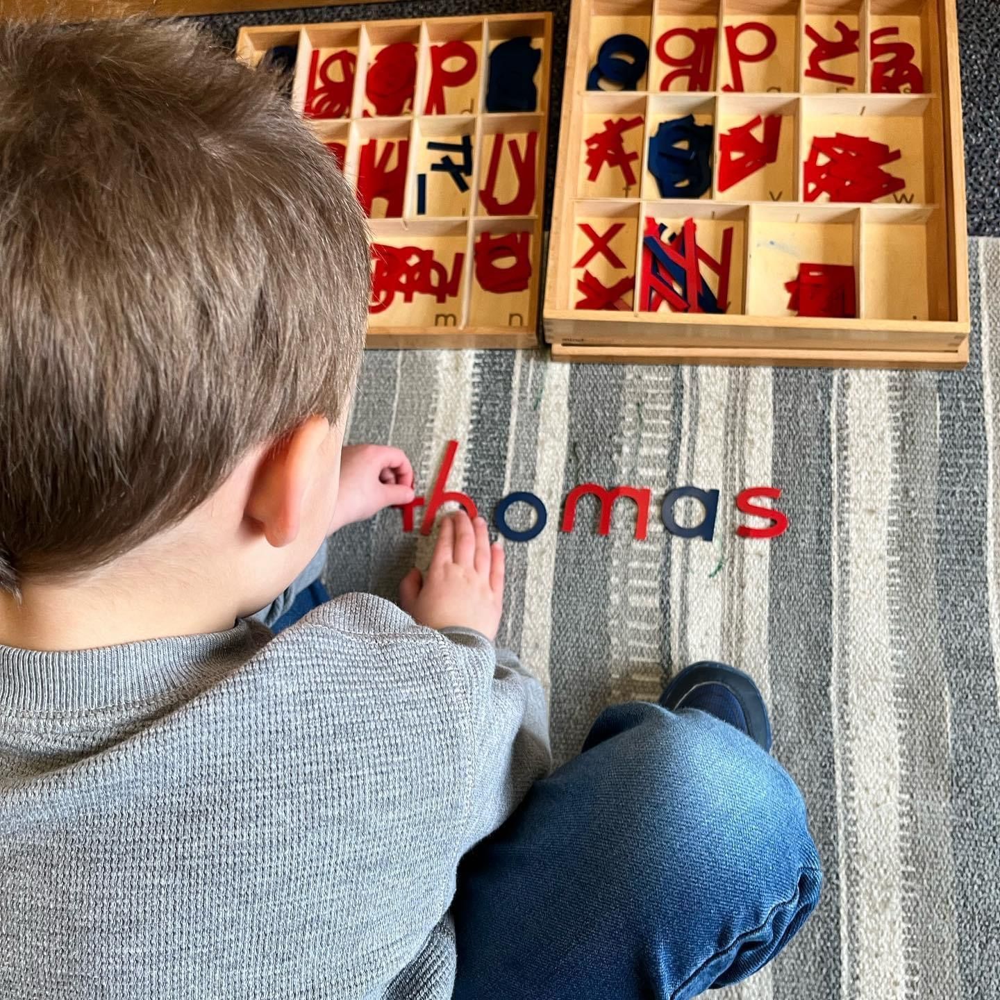 A young boy is playing with letters on the floor and his name is thomas