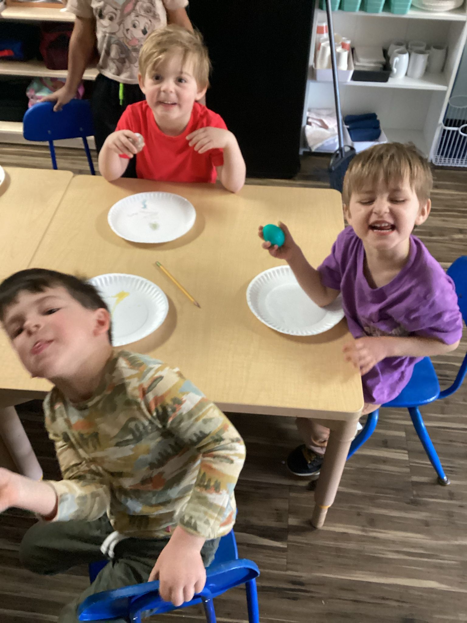 A group of young children are sitting at a table with plates and pencils.