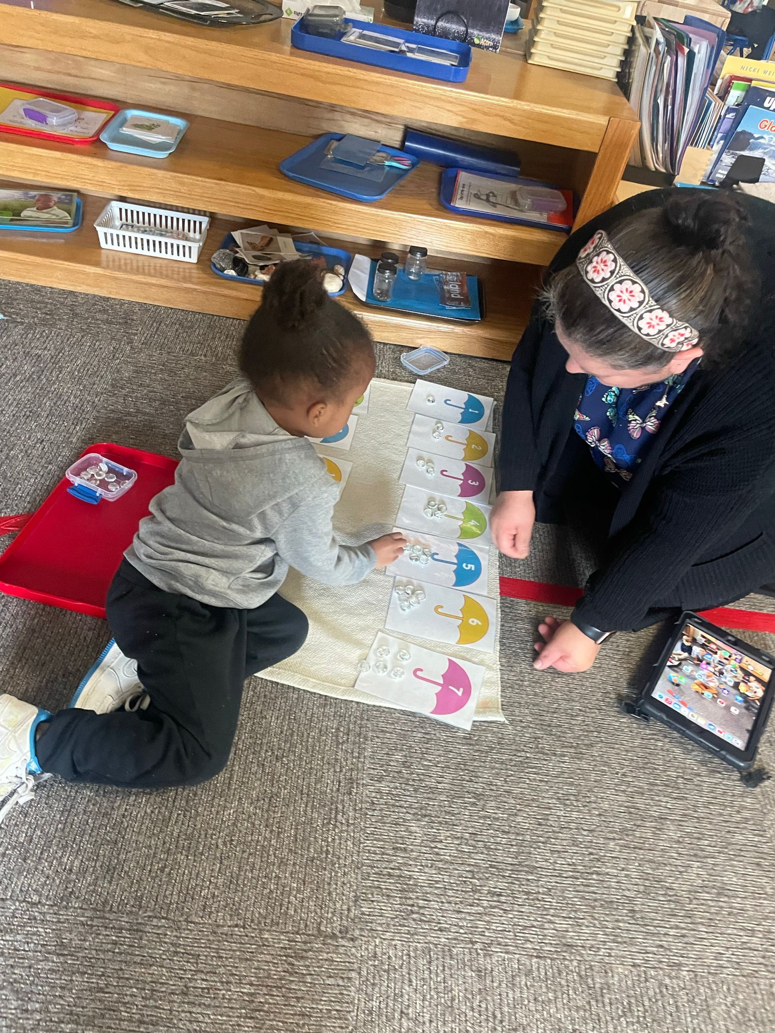 A woman is kneeling down next to a little girl who is playing with a piece of paper.