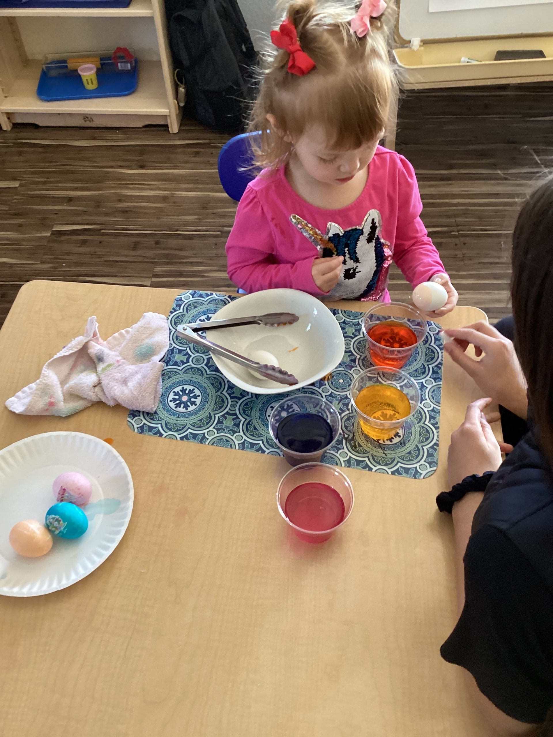 A little girl is sitting at a table painting easter eggs.