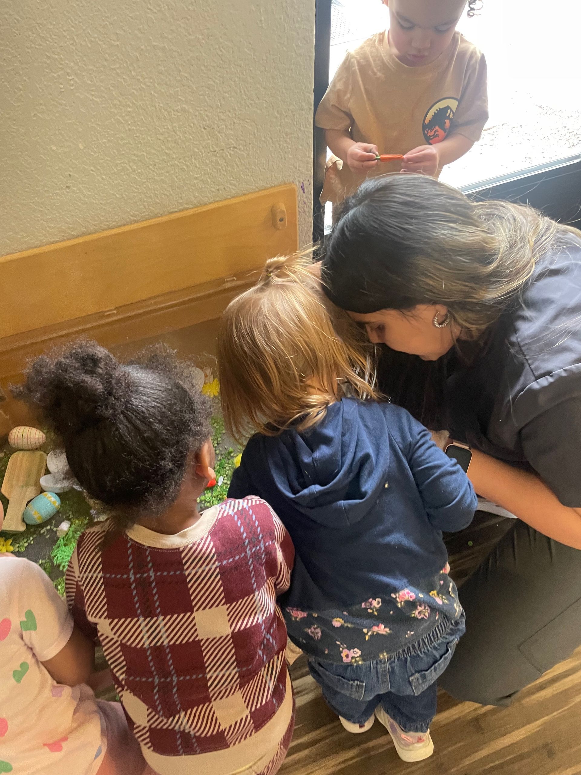 A woman is kneeling down next to a group of children looking at something.