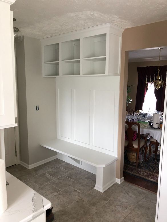 A kitchen with white cabinets and shelves and a bench