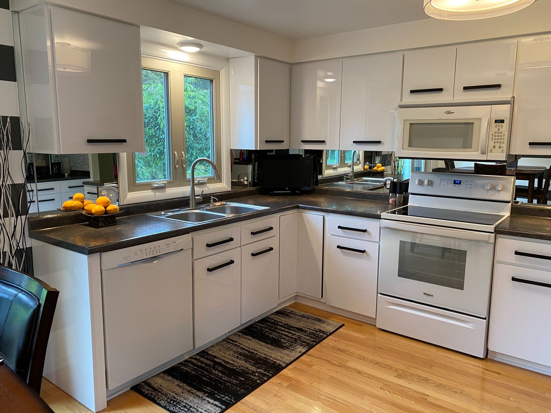 A kitchen with white cabinets , a stove , a microwave and a sink.