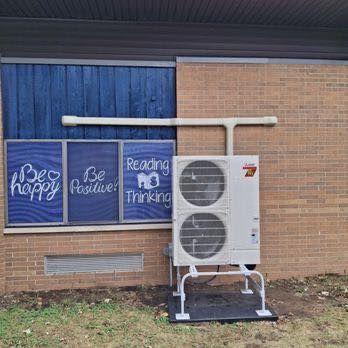 HVAC unit outside a building with a blue wall and windows; chalk writing: 