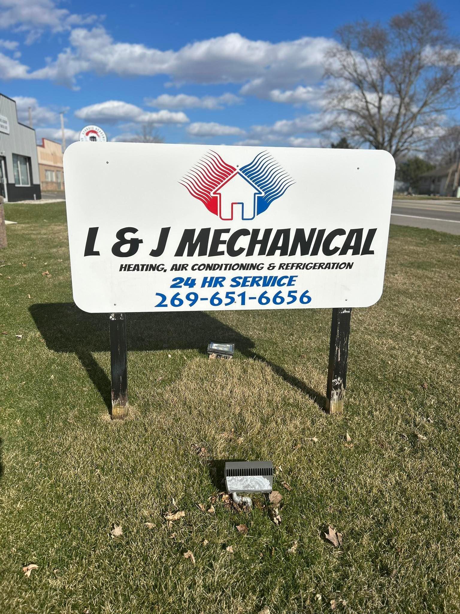L & J Mechanical sign: White sign with company logo, service details, and phone number, set in grassy area.