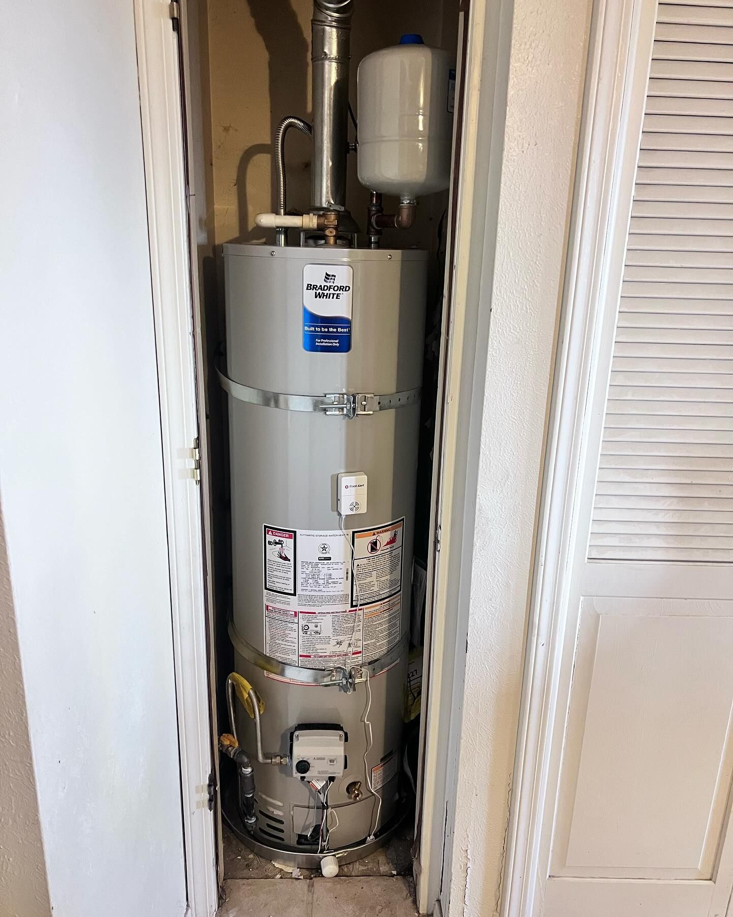 A tall, cylindrical water heater in a closet; white doors, silver tank, vent, and control panel.