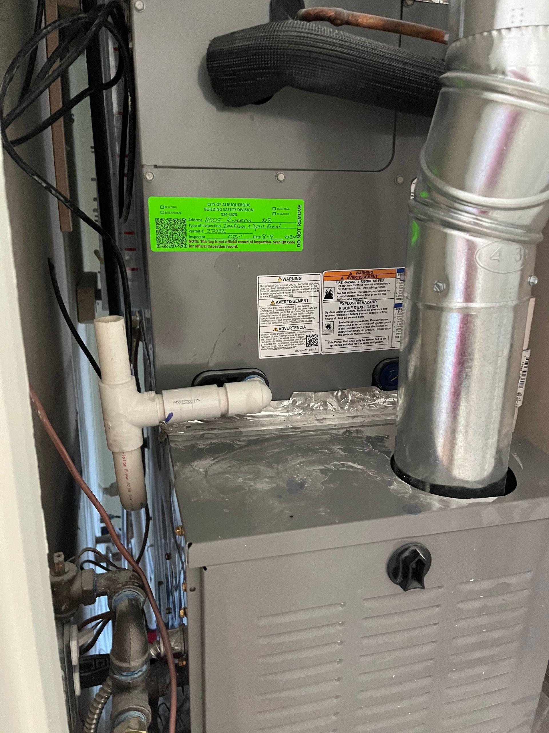 Furnace with connected pipes and vent in a room, showing labels and a black knob.