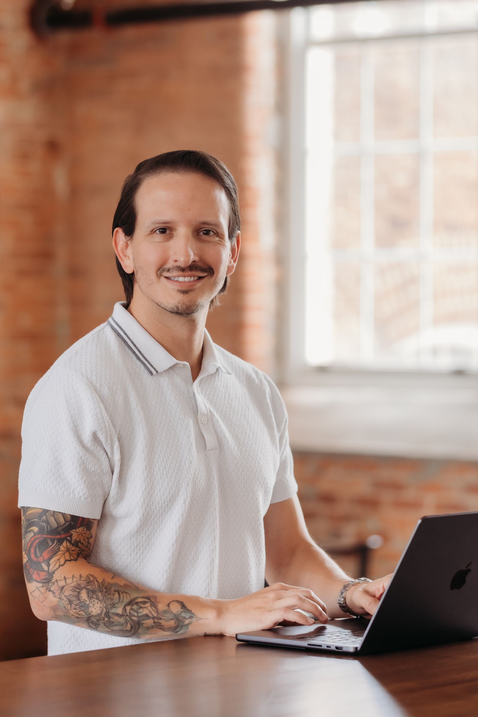 A woman is sitting at a desk with a laptop and a vase of flowers.