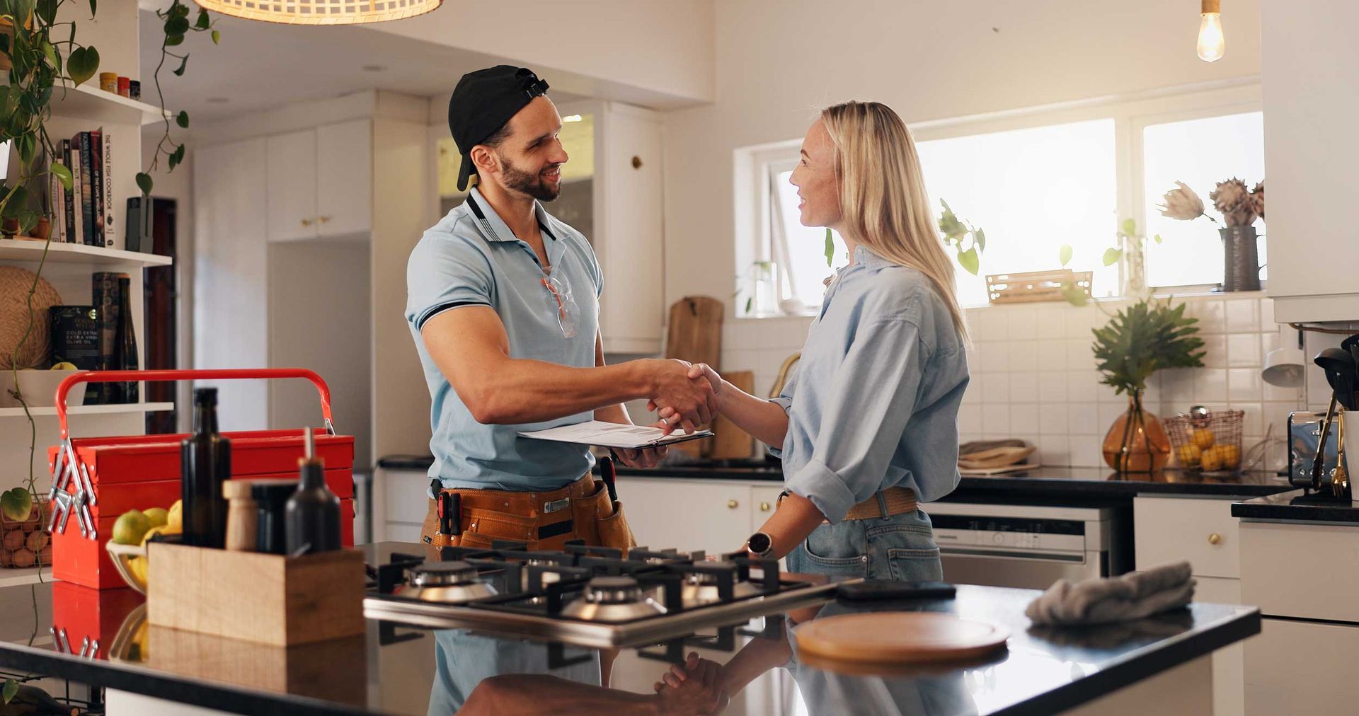 A homeowner shaking hands with a plumber in a kitchen after completing a repair service