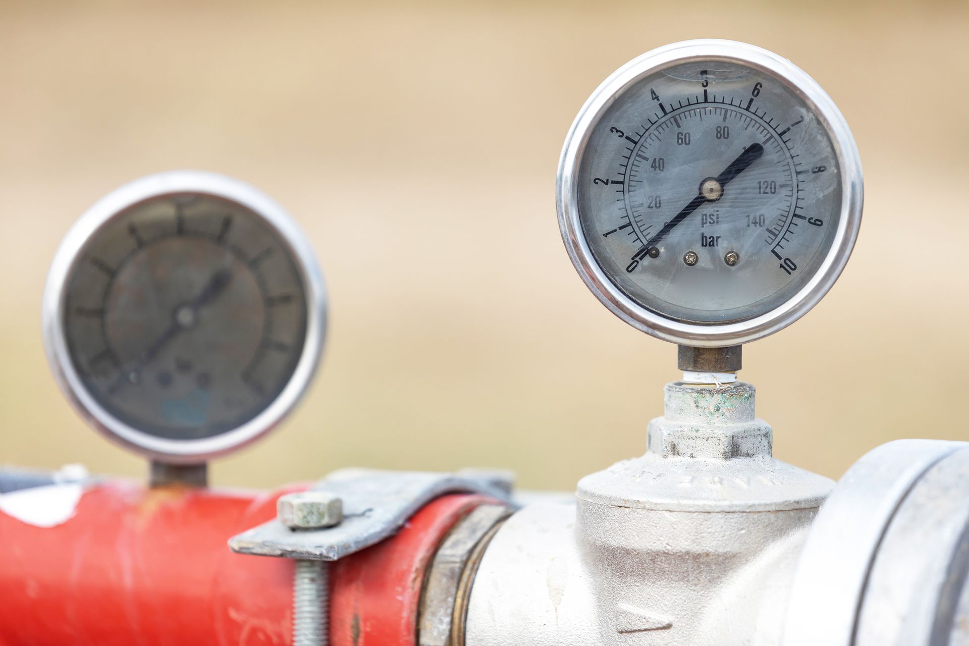Two pressure gauges mounted on a pipe, one red and the other silver. The gauges have black needles pointing to various pressure readings.