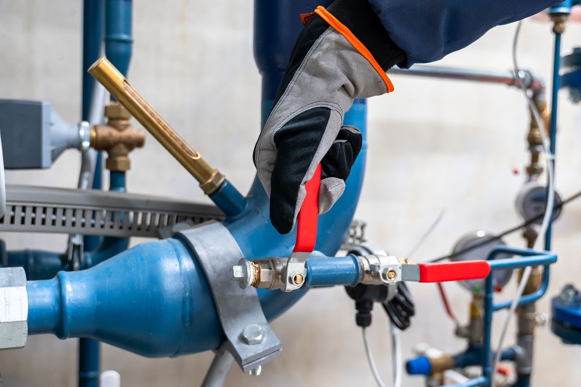A gloved hand turning a red valve on a blue pipe in a machinery room.