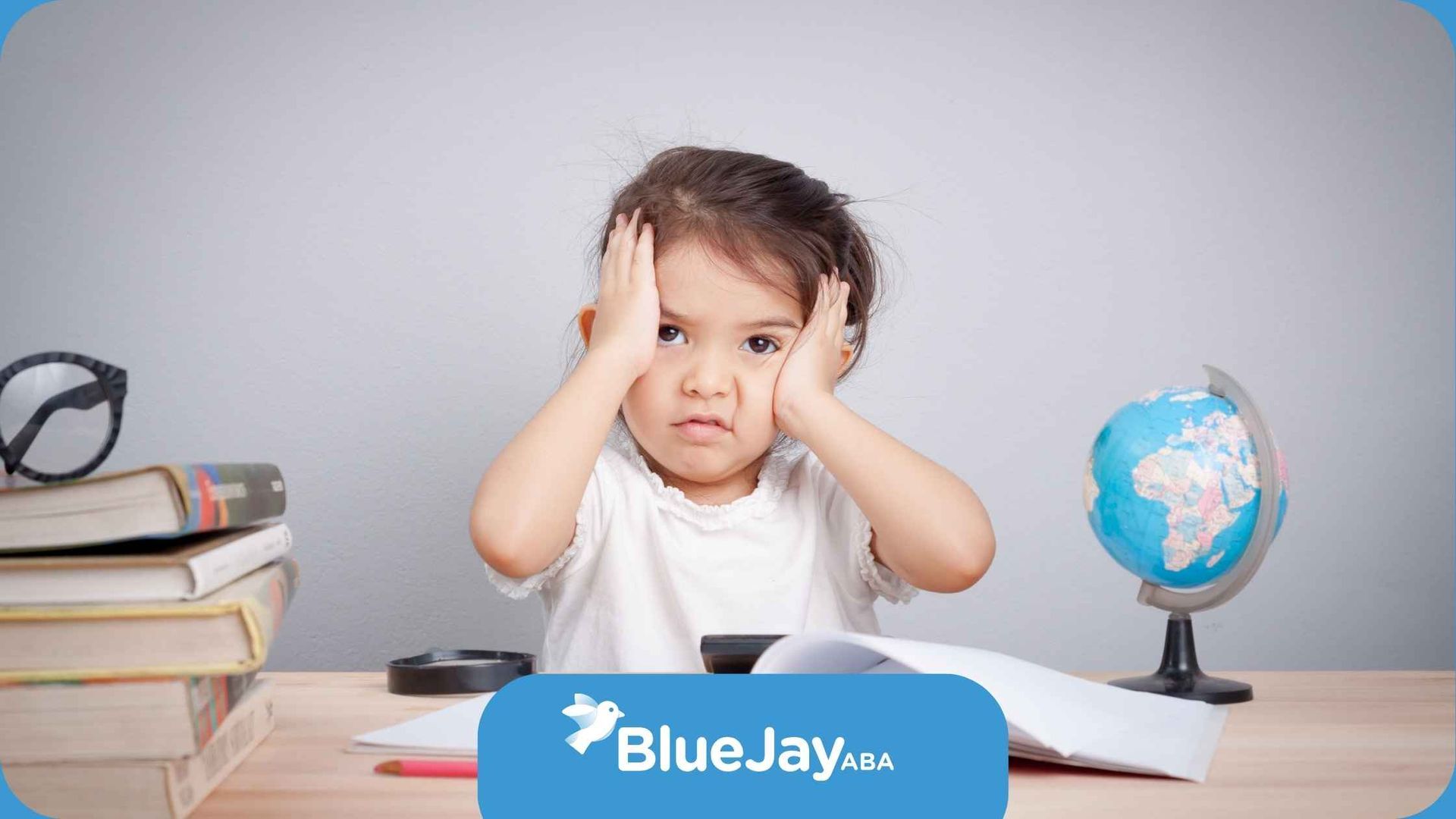 A little girl is sitting at a desk with books and a globe.