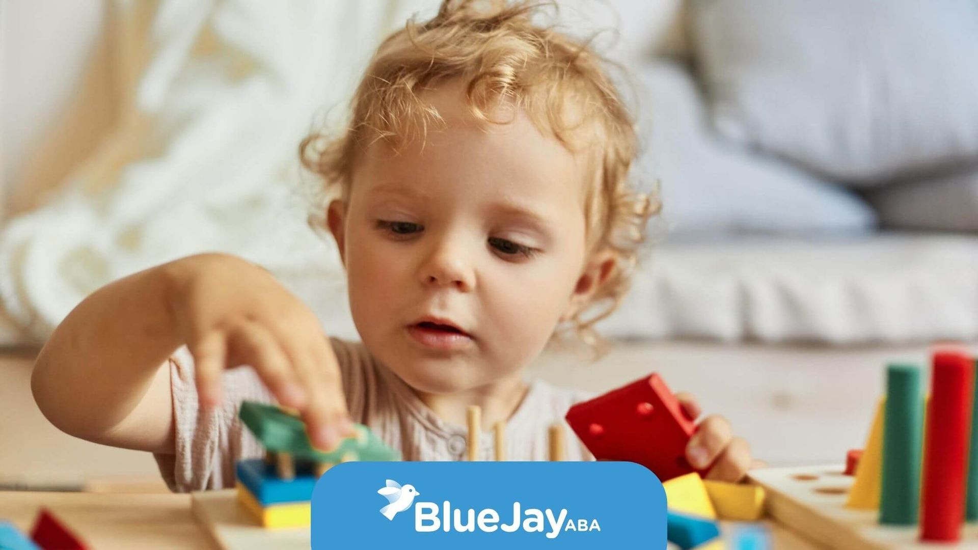 A toddler building with colorful blocks in a playroom during ABA therapy.