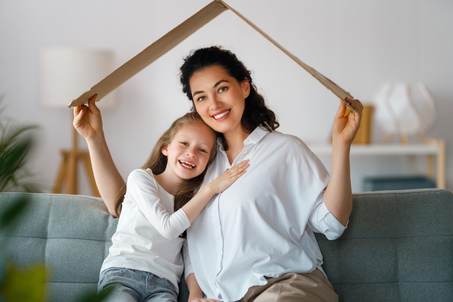 A woman and a little girl are sitting on a couch holding a cardboard house.