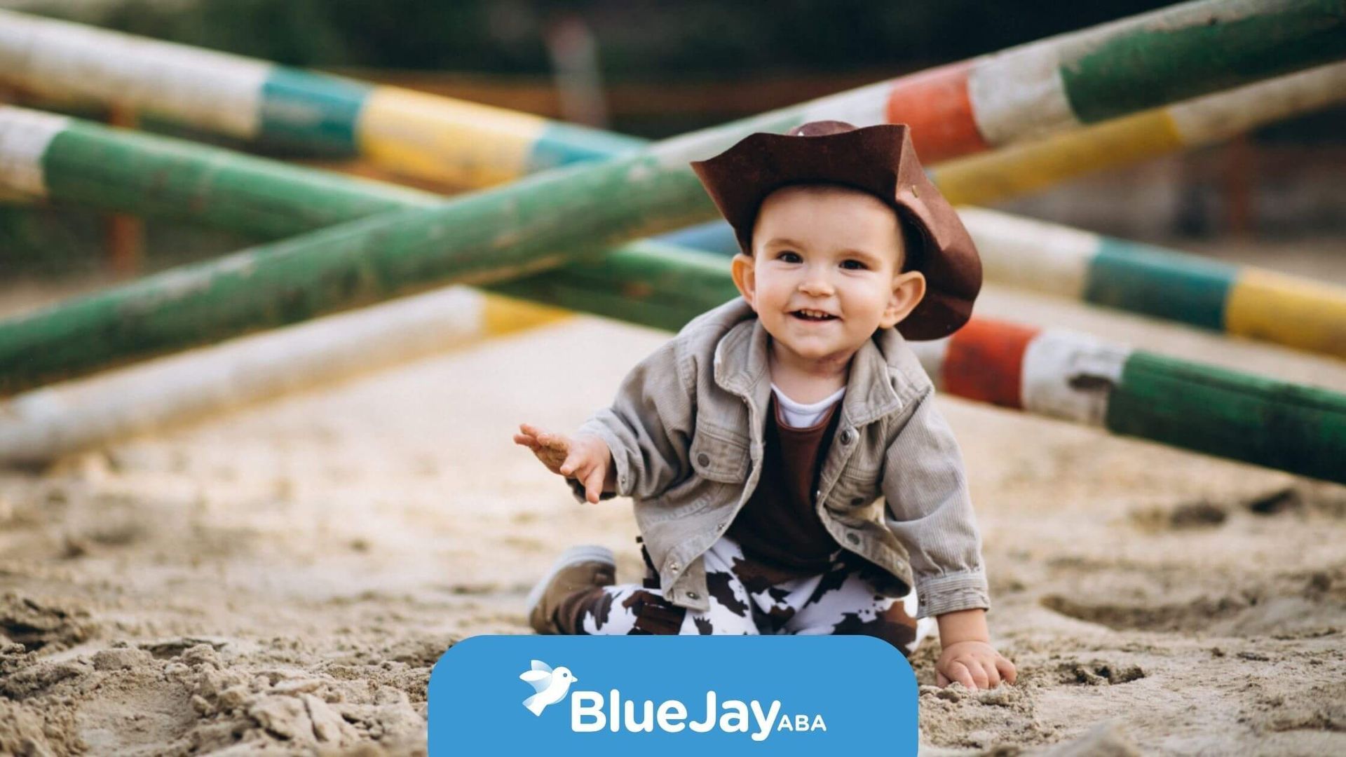 A young child with autism dressed in a cowboy hat, playing in the sand at an outdoor park.