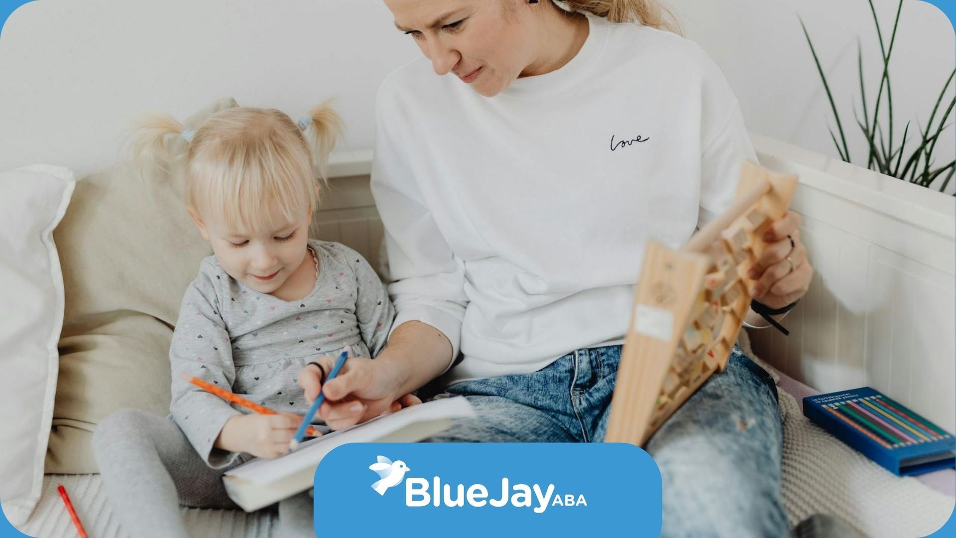 An ABA therapist and autistic child drawing together on the couch during in-home ABA therapy in NC.