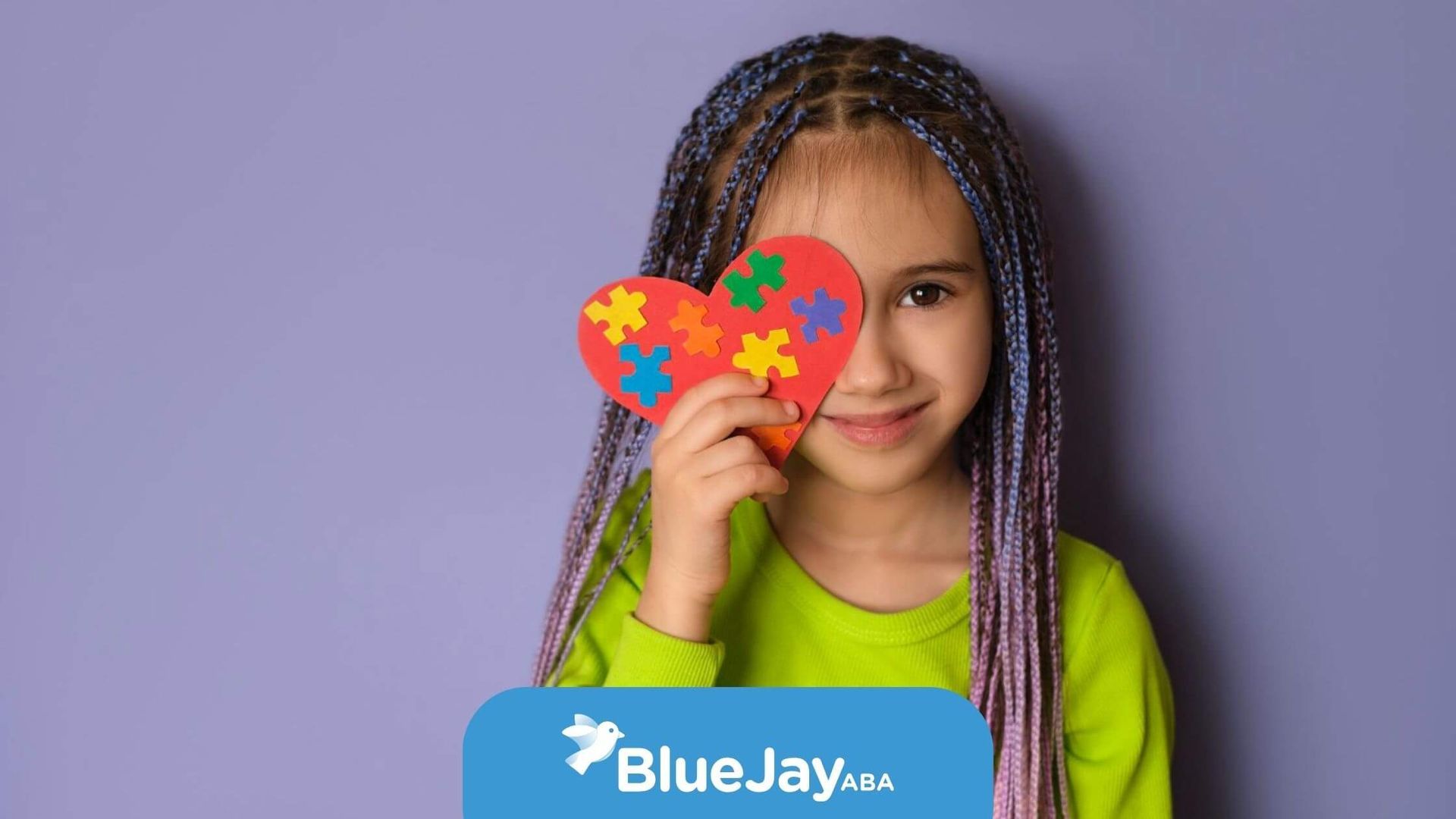 Child with autism holding a colorful heart-shaped puzzle piece over one eye.