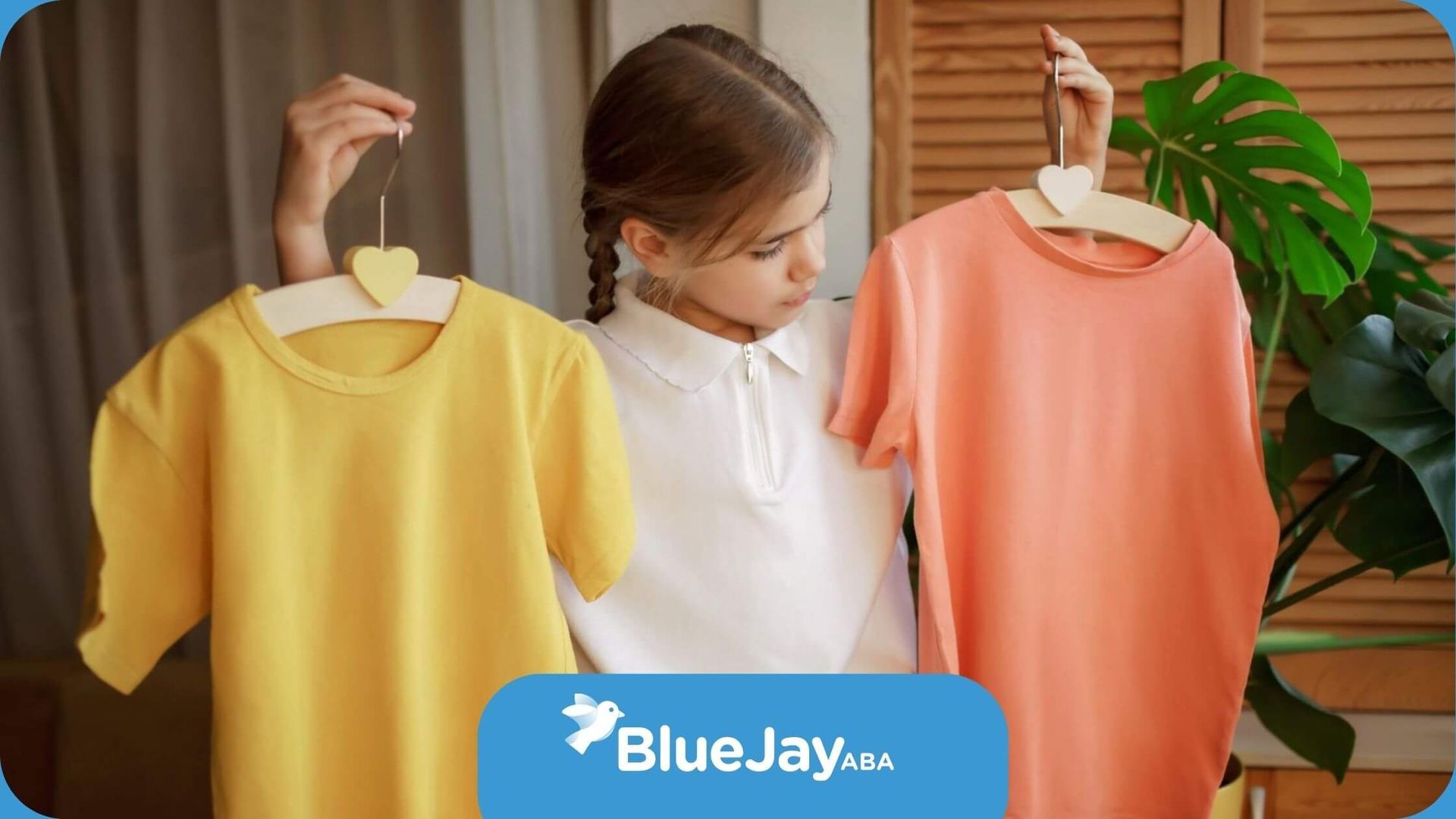 A child with autism holding up two T-shirts, one yellow and one orange.