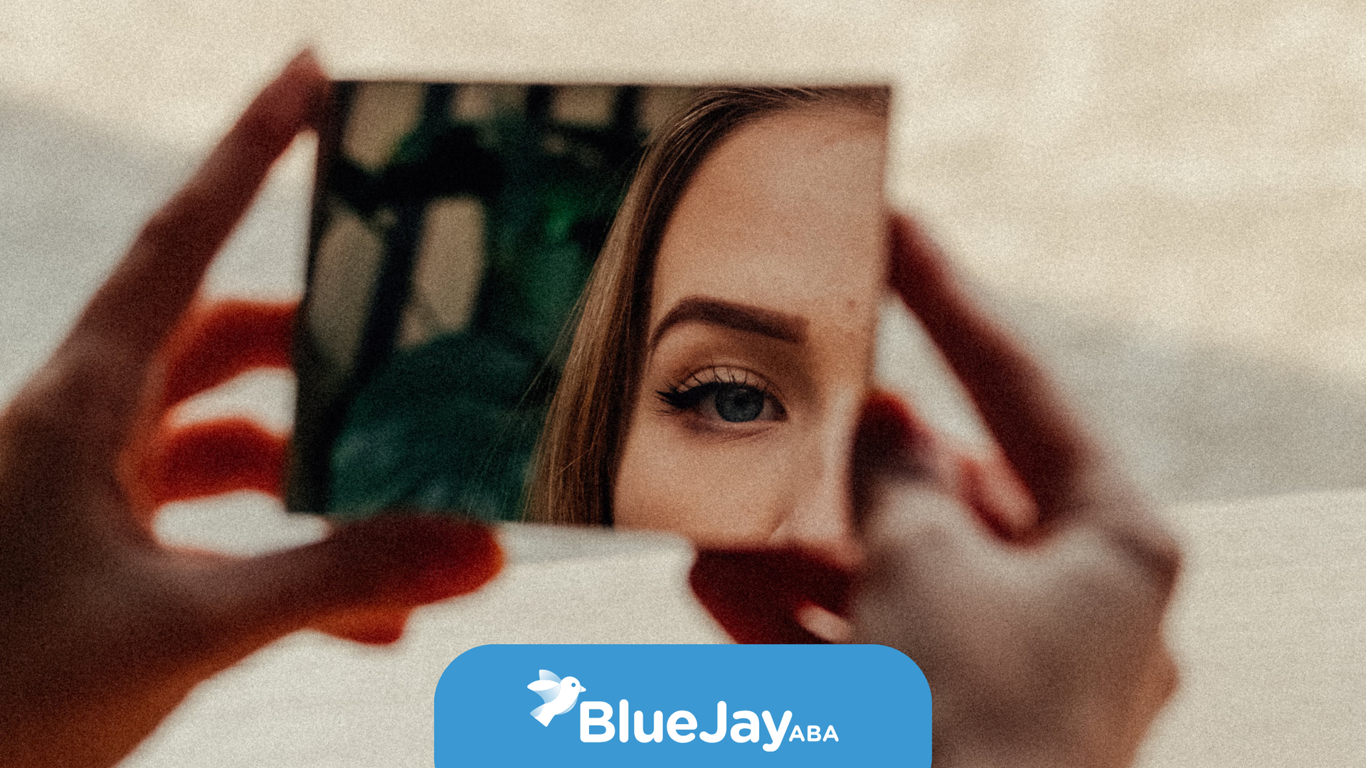 Hands holding a small square mirror reflecting a woman's eye and part of her face.