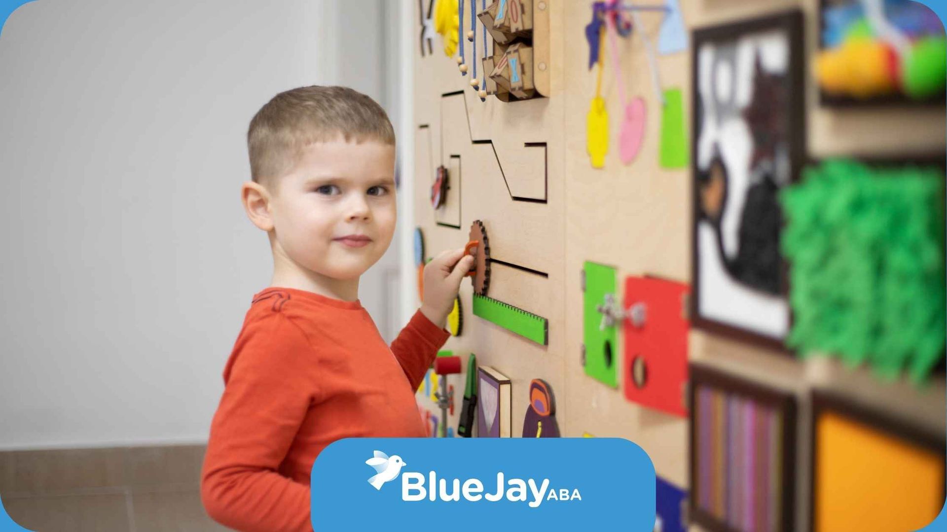 A young boy is playing with a busy board on a wall.