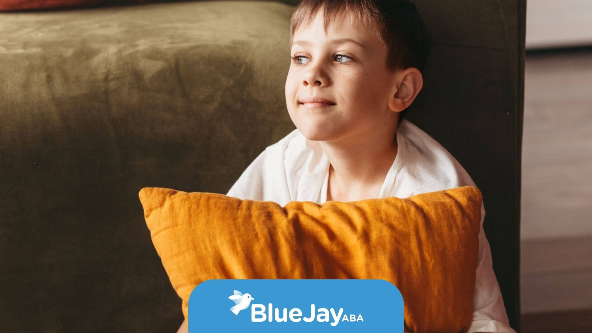 Young boy sitting on a couch holding an orange pillow in ABA therapy.