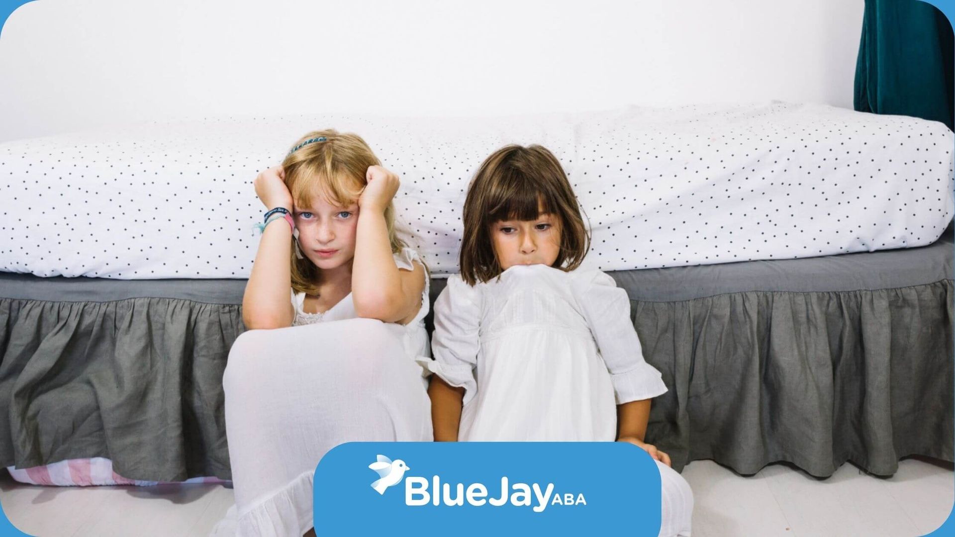 Two little girls are sitting on the floor next to a bed.