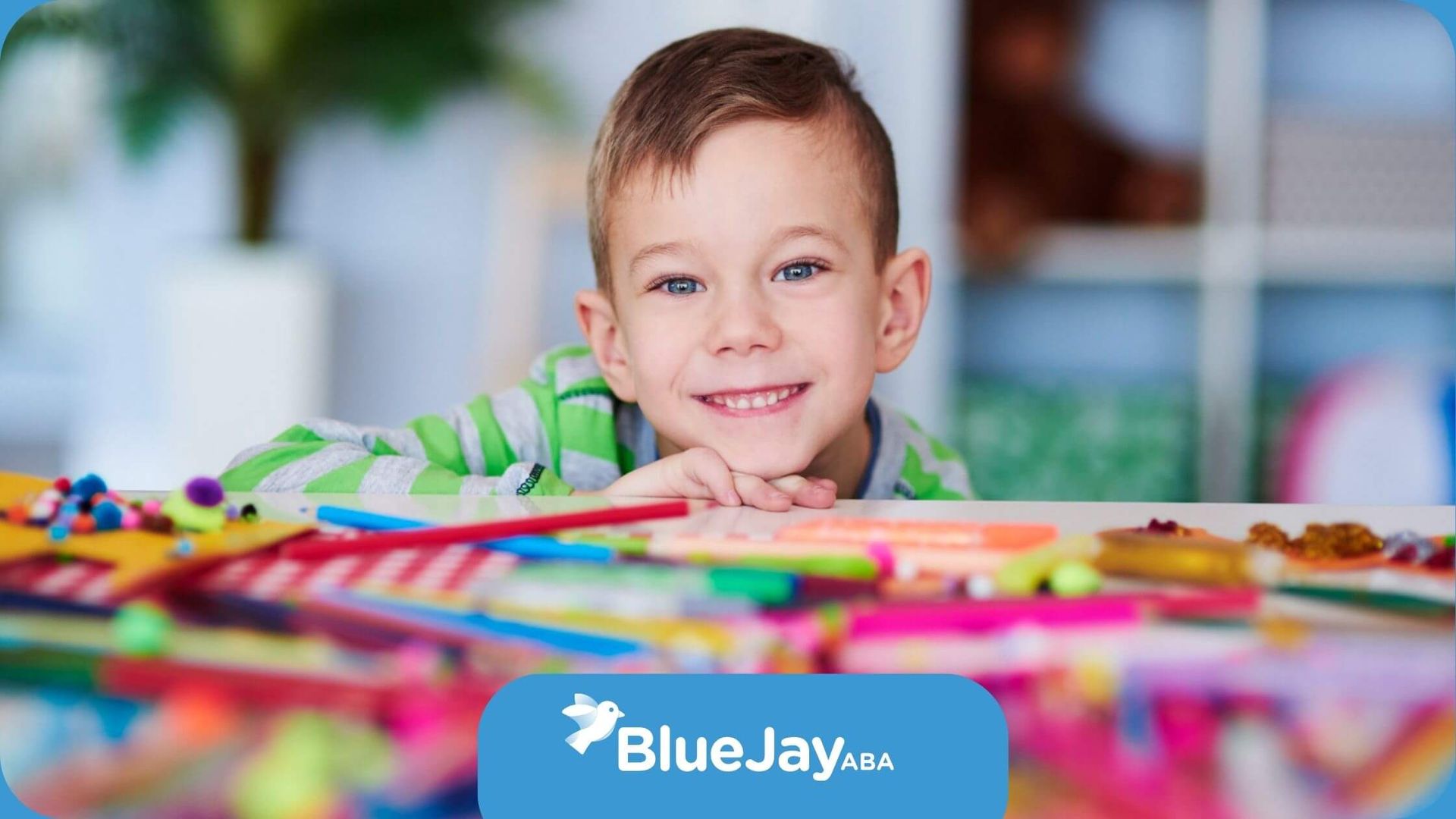 A young boy with autism is sitting at a table with a pile of colored pencils.
