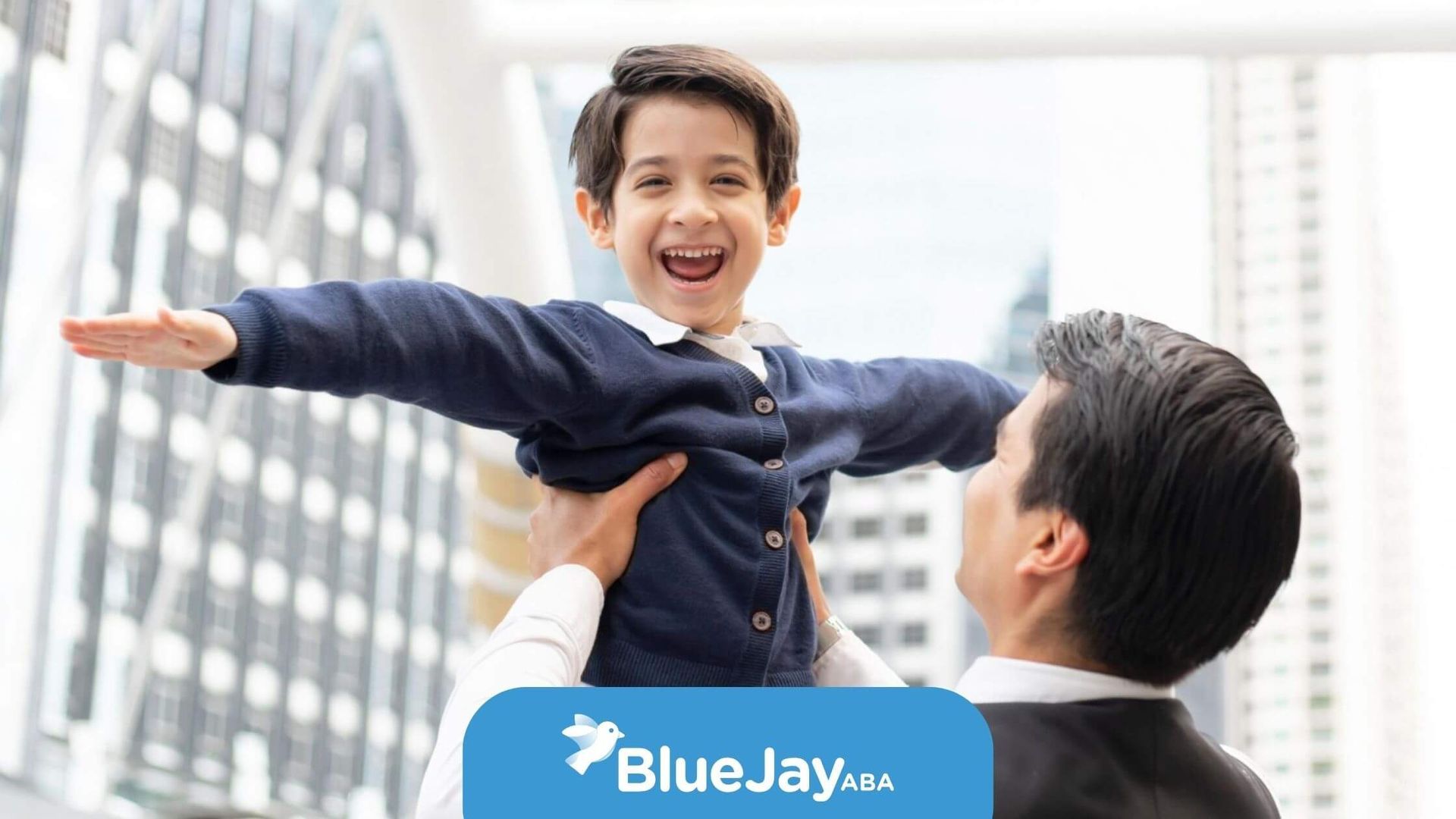 A joyful young boy with autism being lifted in the air by a BCBA outdoors.