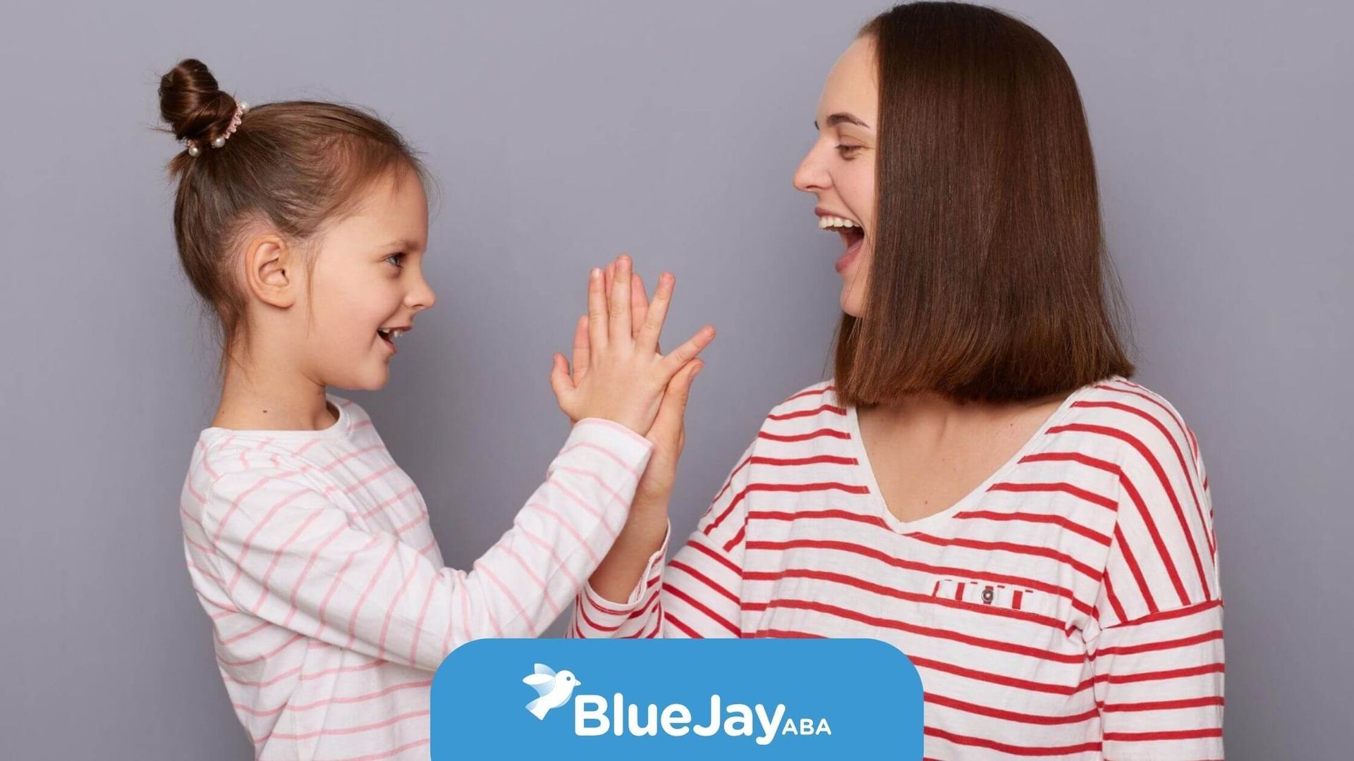 Young girl and BCBA smiling and playing a hand-clapping game in ABA therapy.