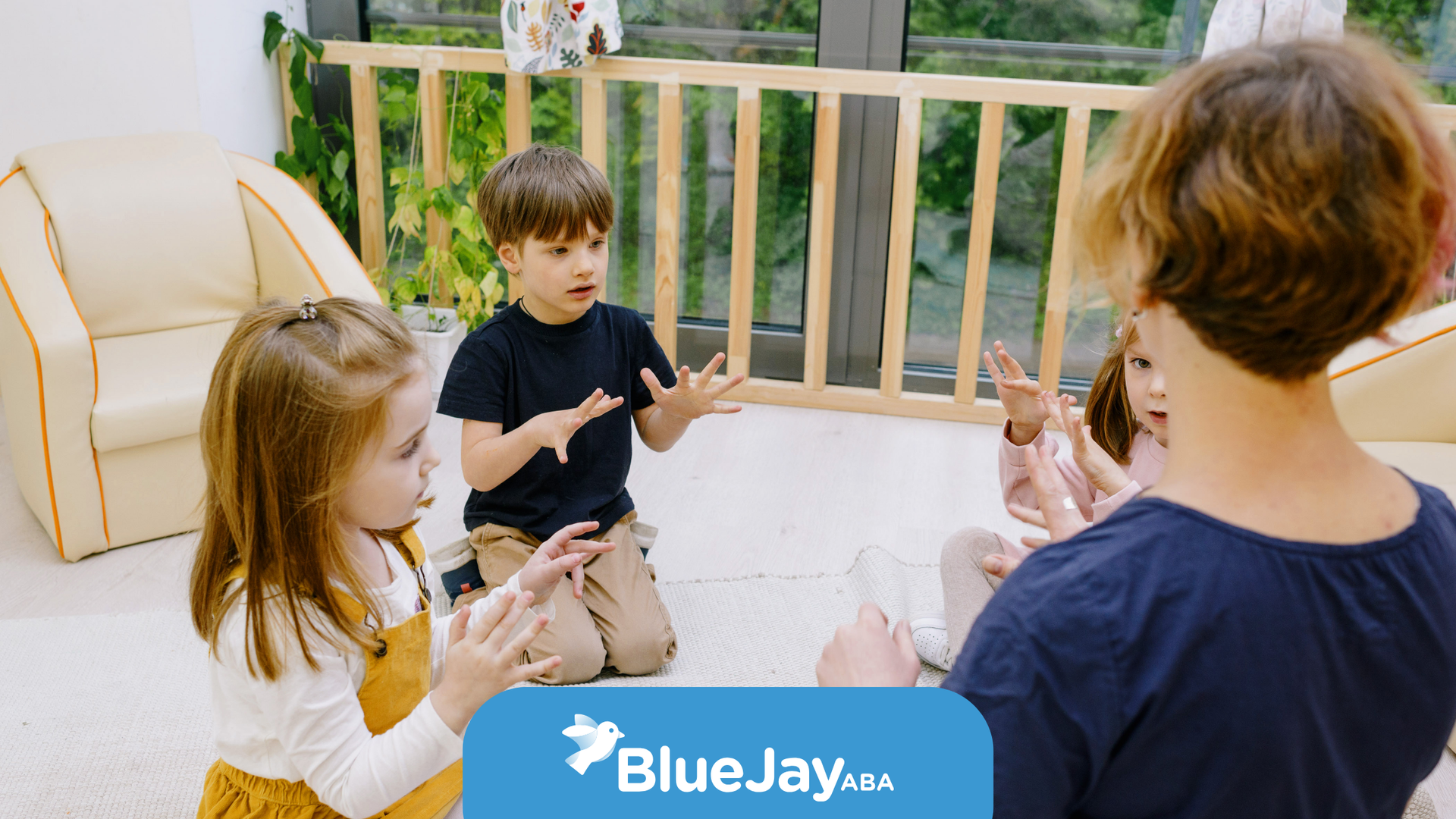Children and teacher in a brightly lit room, clapping and playing.  BlueJay logo in the corner.