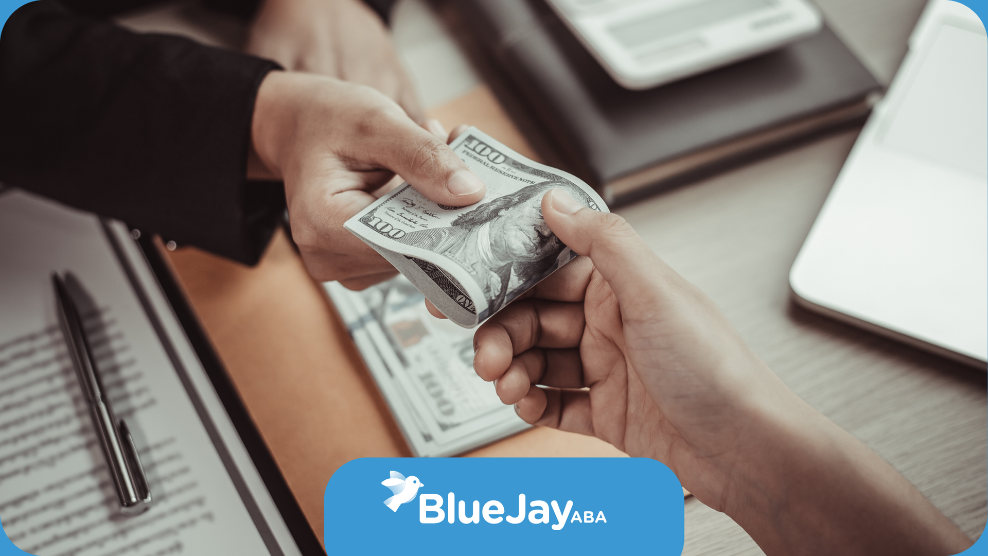 Hands exchanging money over a desk with paperwork, suggesting a transaction.