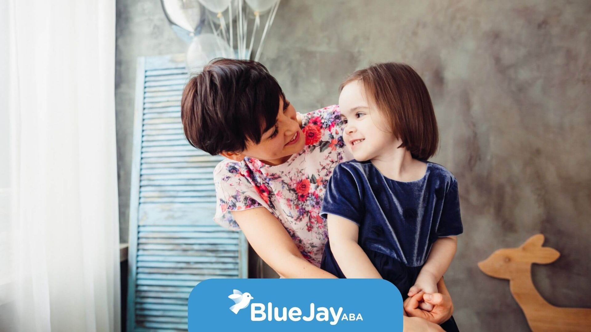 BCBA hugging young child with autism indoors near window.