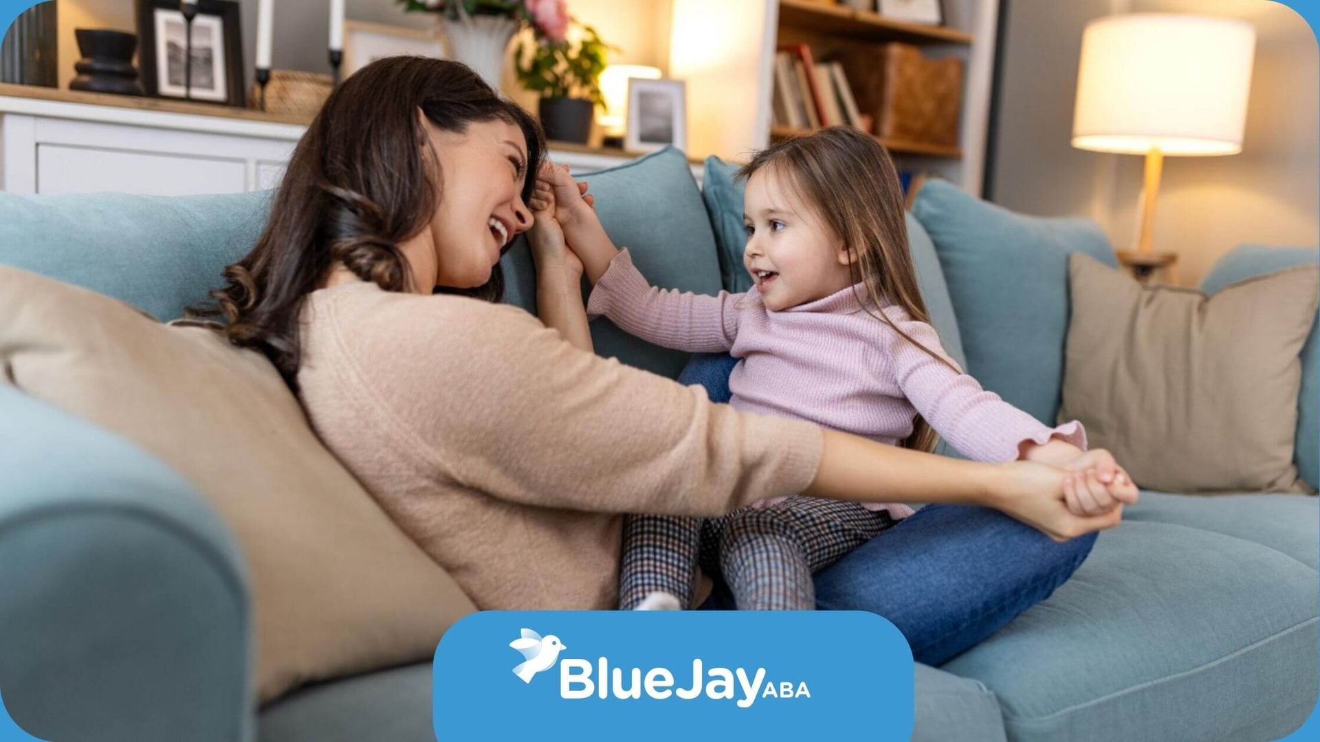 ABA therapist and autistic girl laughing together on a couch in ABA therapy.