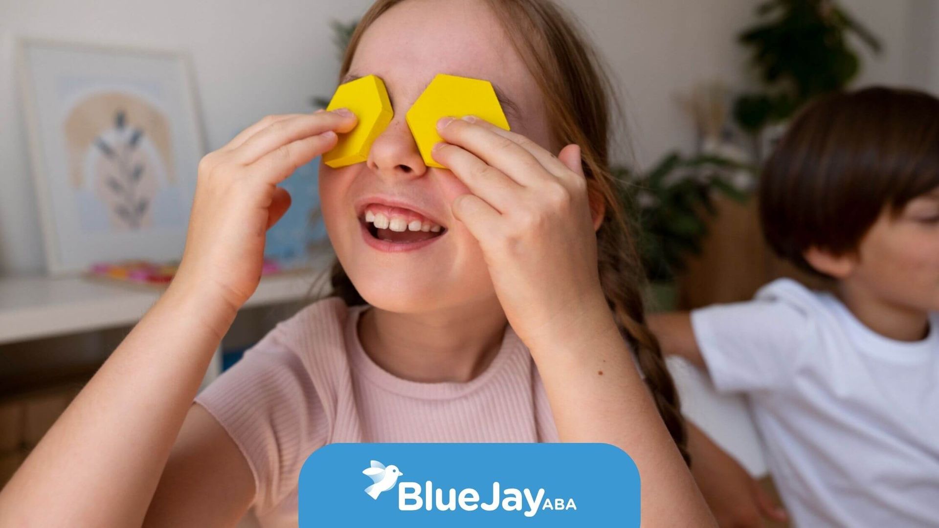 Child with autism smiling while holding yellow shapes over their eyes during play.