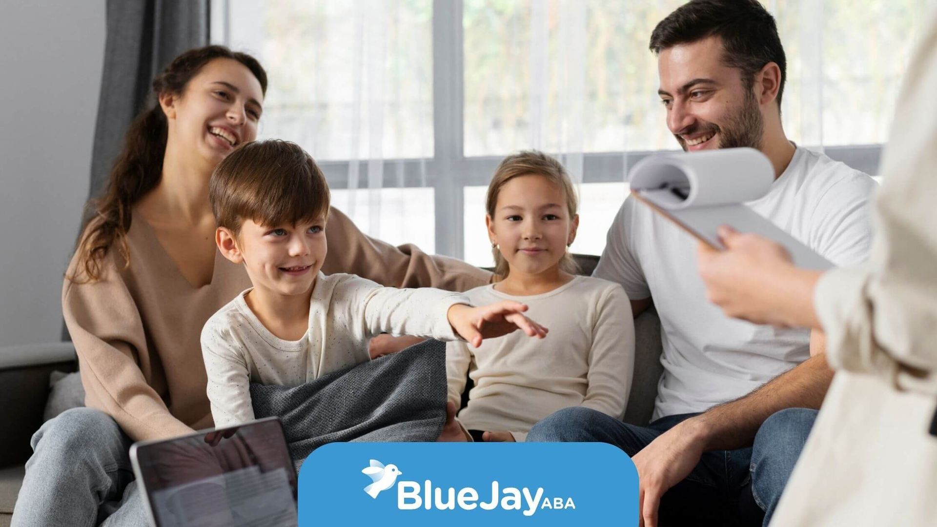 A family of four sitting on a couch, the children are smiling, and one of them is reaching out.