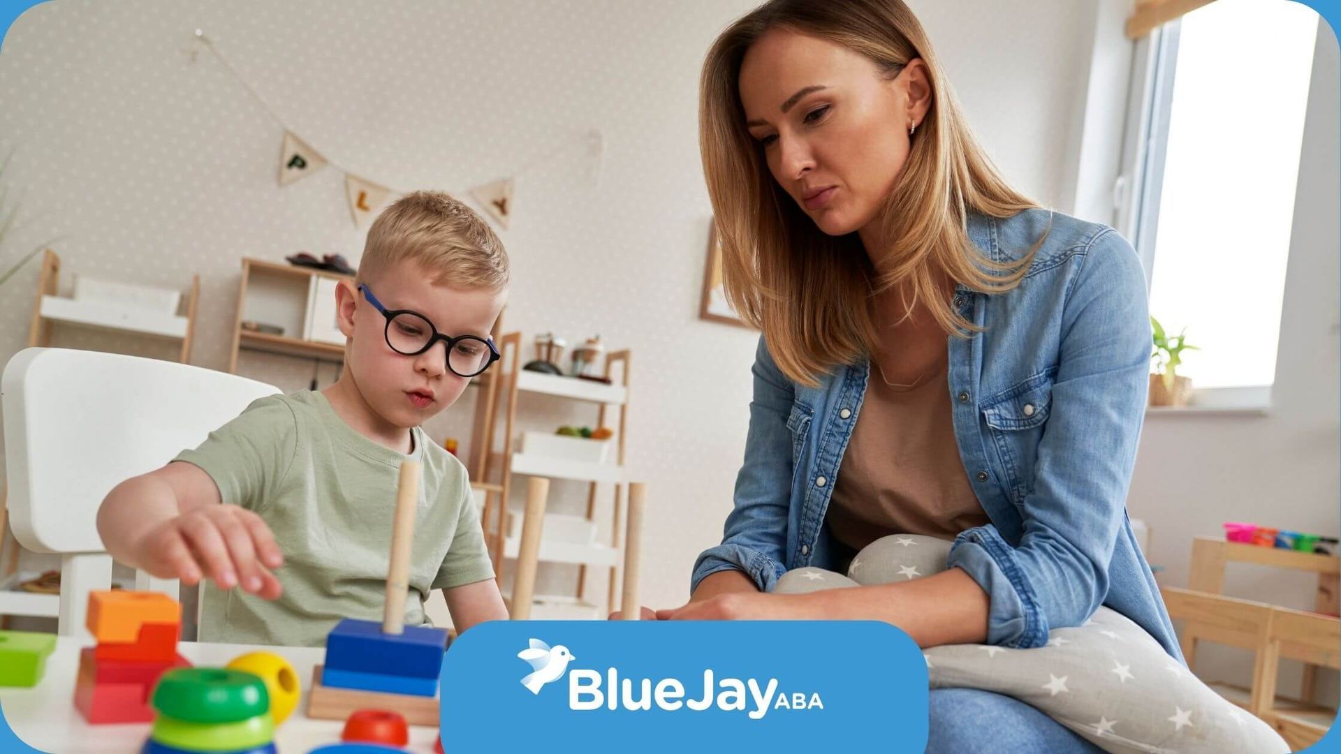 An ABA therapist is sitting next to a young boy playing with blocks in ABA therapy.