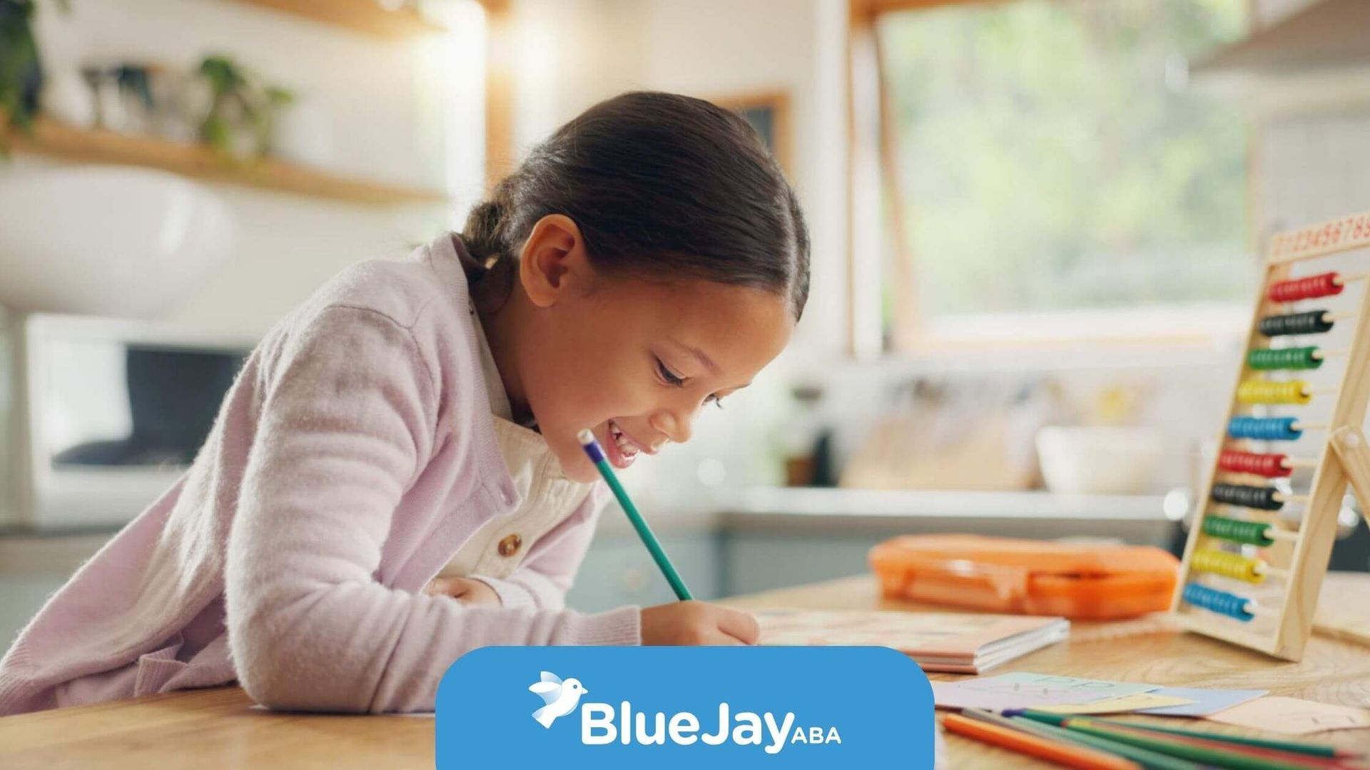 Smiling girl with autism drawing with colored pencils at a kitchen table during ABA therapy.