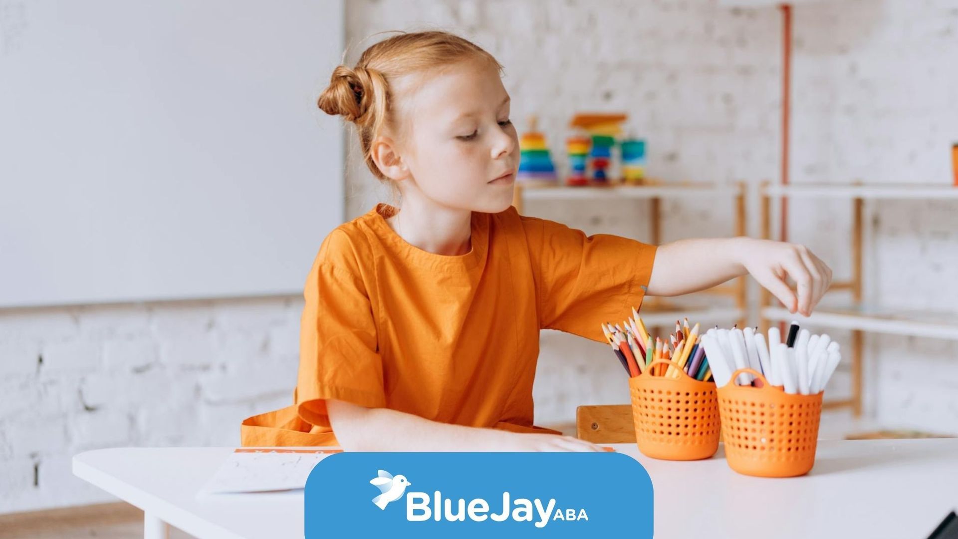 Autistic girl in orange shirt picking markers from a basket during school-based ABA therapy in NC.