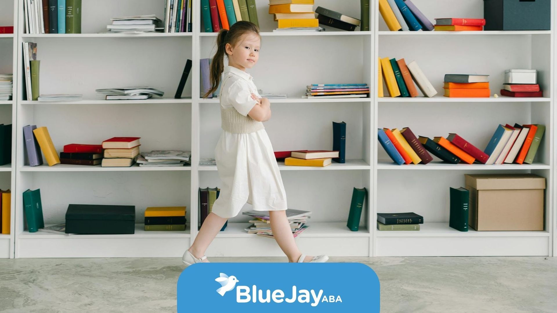 Autistic girl in a white dress standing in front of bookshelves with books during ABA therapy in NC.