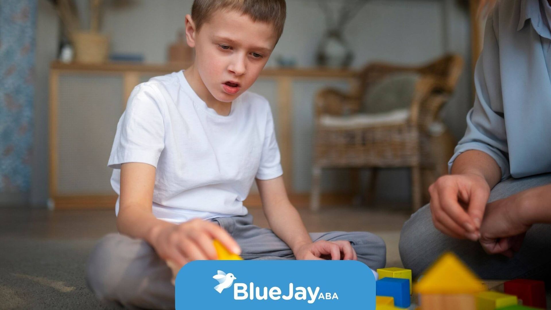 A boy is playing with colorful building blocks, with an adult sitting beside him assisting.